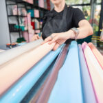 Florist chooses roll of paper for bouquet of flowers. Woman working in flower shop. Cropped photo
